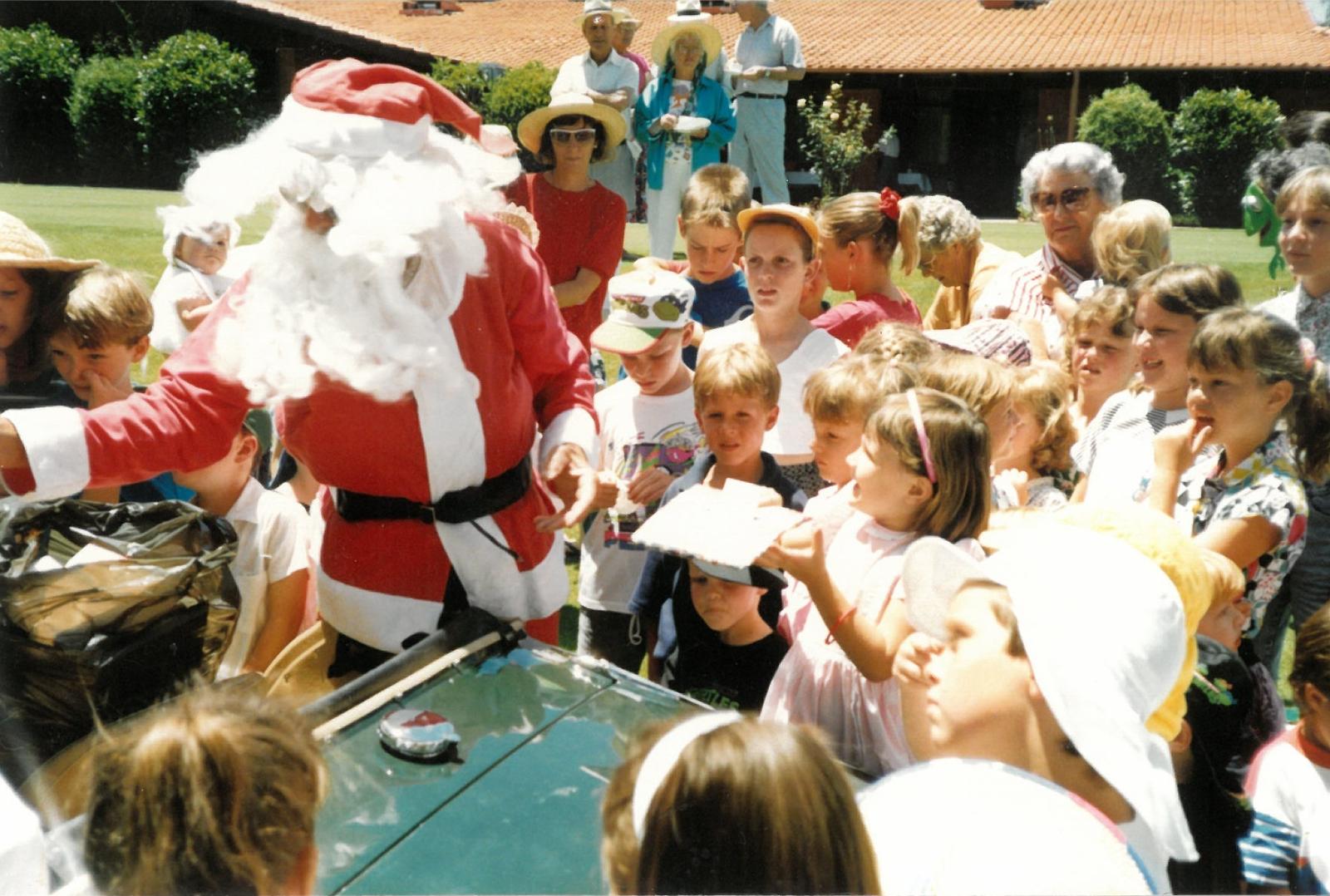 Santa Claus in a red suit and white beard surrounded by children at a party at Melville Glades Golf Club clubrooms.