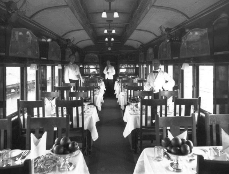 interior black and white photo of dining car with tables set and wait staff c1920