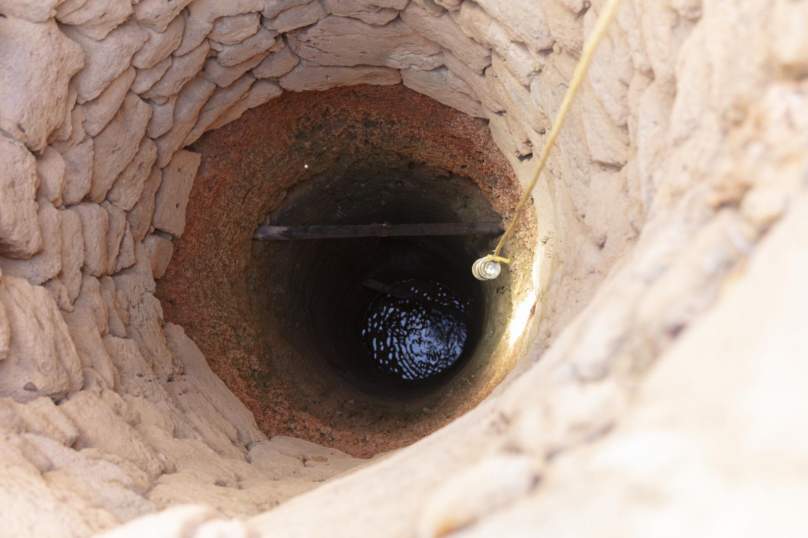 Looking down into the well, light shining on water at bottom.