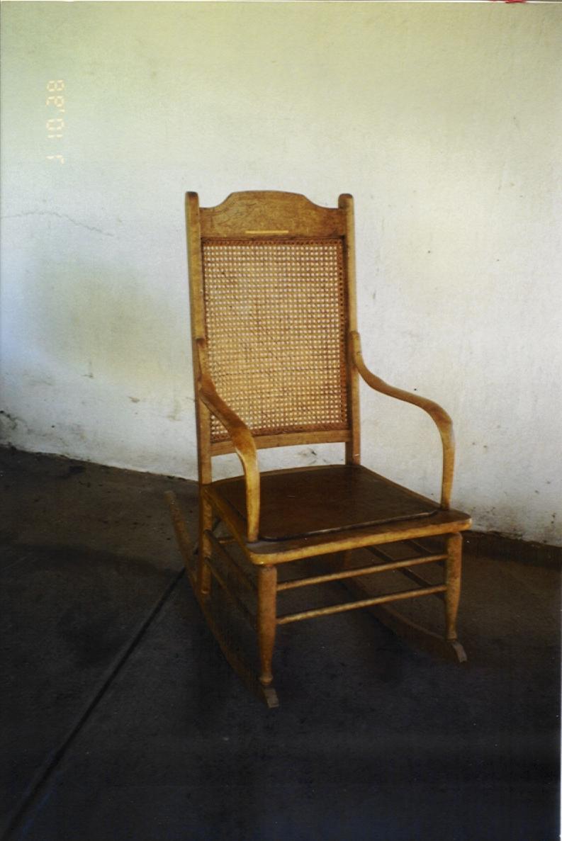 Rattan chair on dark wood floor with cream wall behind.