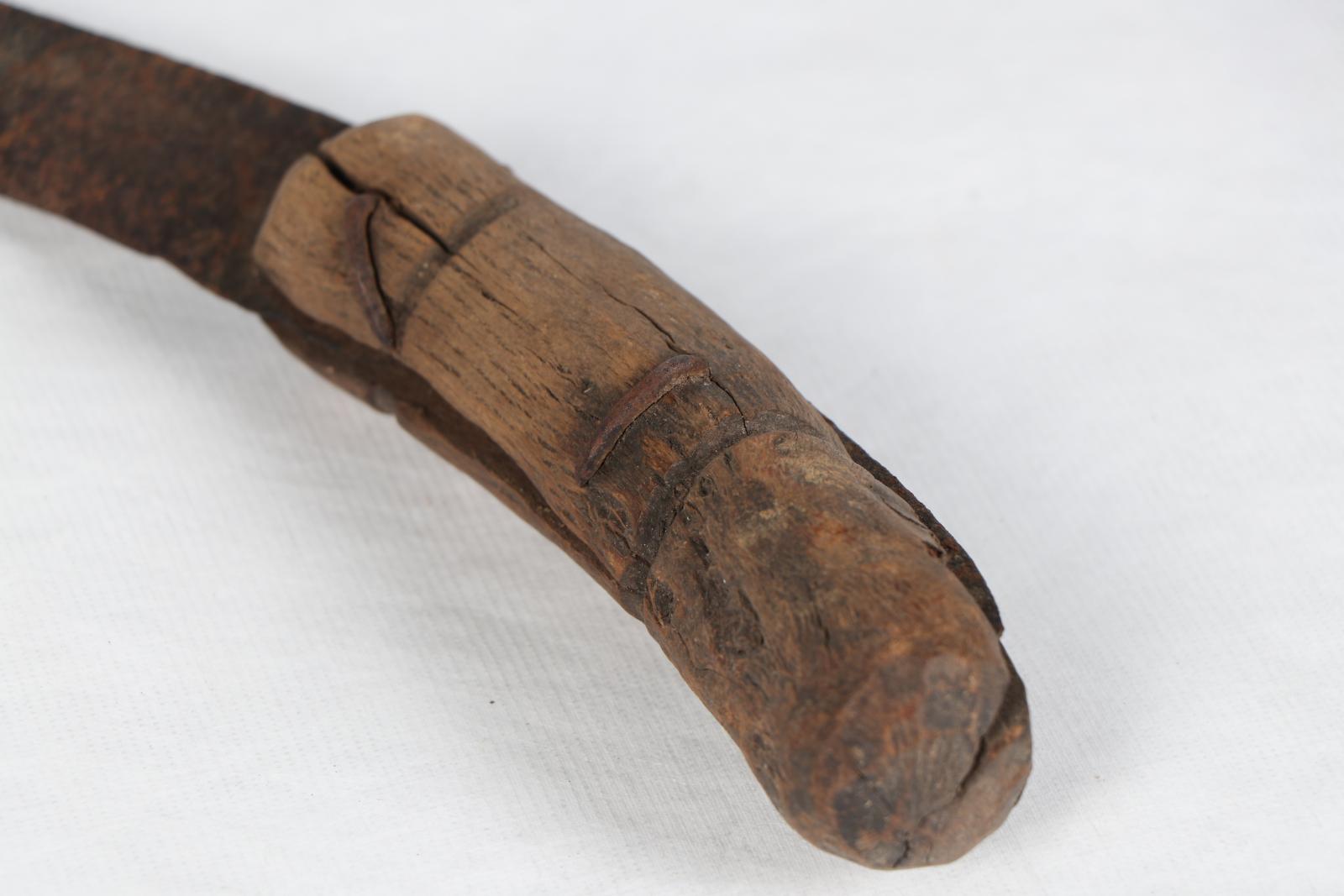 Close up of wooden handle of sickle, which is split and rough.