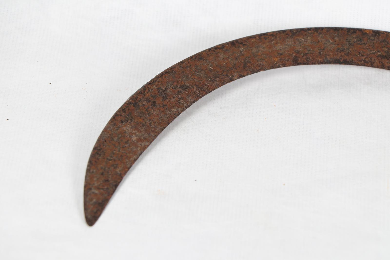 Close up of sickle's pointy end, which is very rusty.