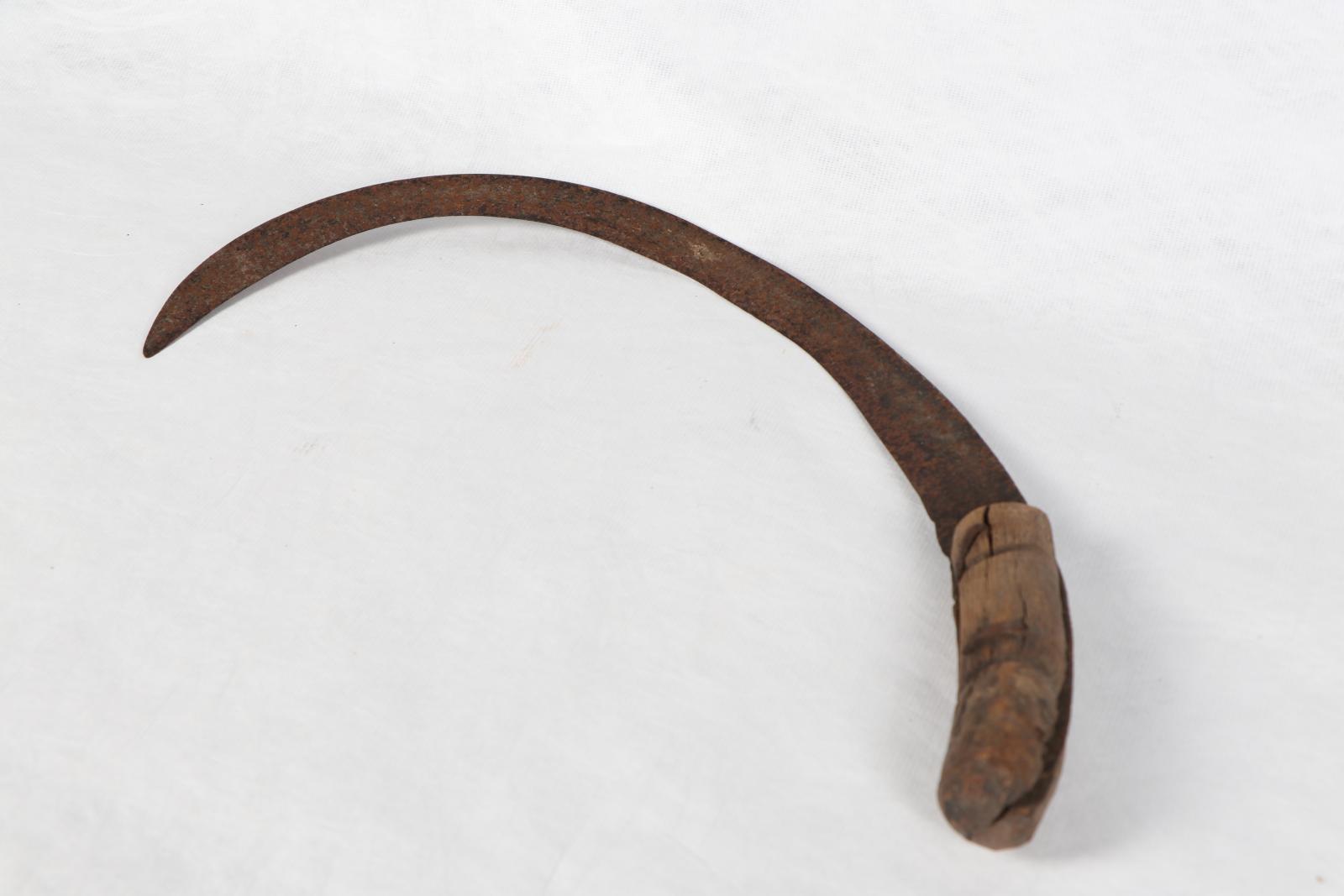 Sickle with metal blade and crude wooden handle against white background.