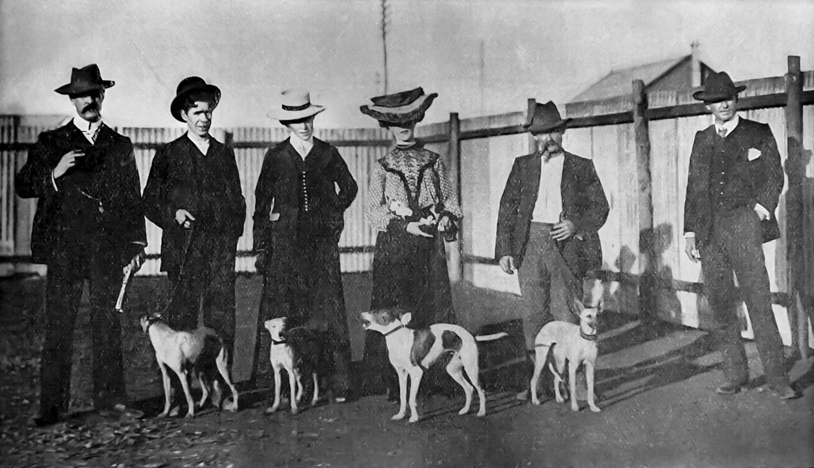 Four men and two women stand with four whippets on leads.