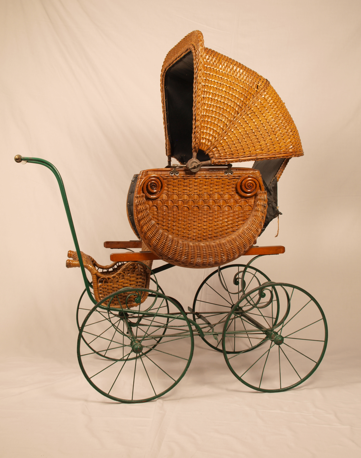 Side view of wicker pram with hood up and green metal spoked wheels.