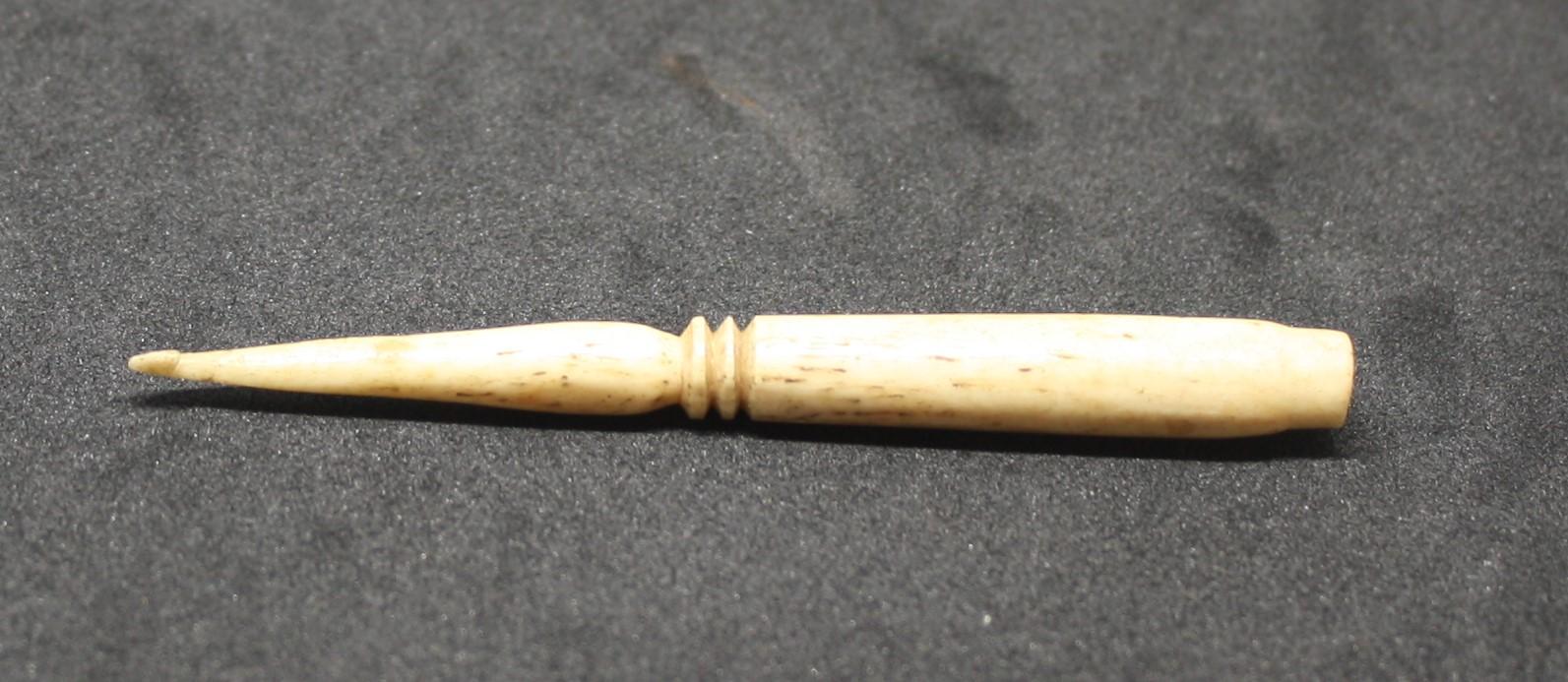 cream bone crochet tool, round body, tapers to a point at one end with a small hook. Two circular ridge decorations have been lathed in the middle