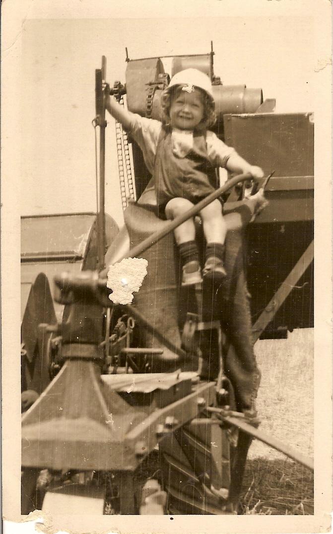 Black and white photograph of a young boy sitting on a harvester