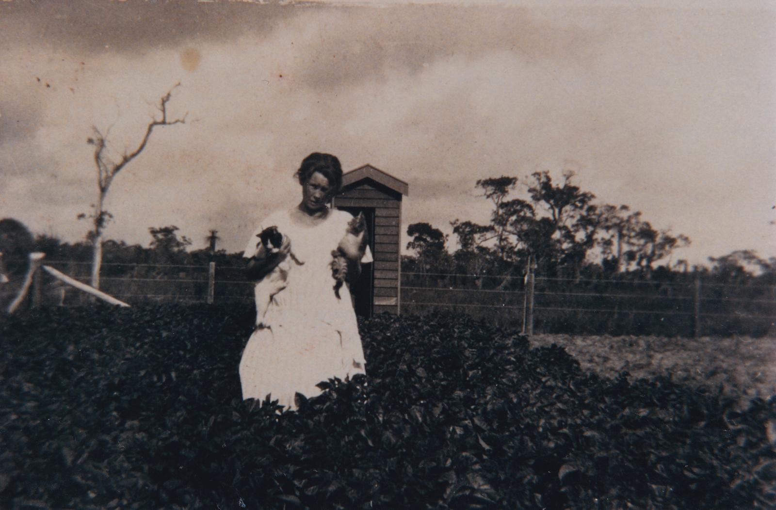 Mrs Lilly Coates holding her cats in the potato patch at Group 52. 