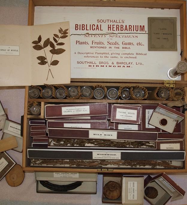 Photo shows old wooden box open.  Writing on the inside Southalls Biblical Herbarium.  Small book of plants in the bible is placed against the lid.  The box contains a number of glass containers and cardboard containers