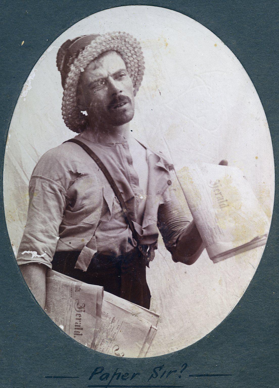 P100-39. Unknown man posing as a paper seller. Caption reads 'Paper Sir?'.