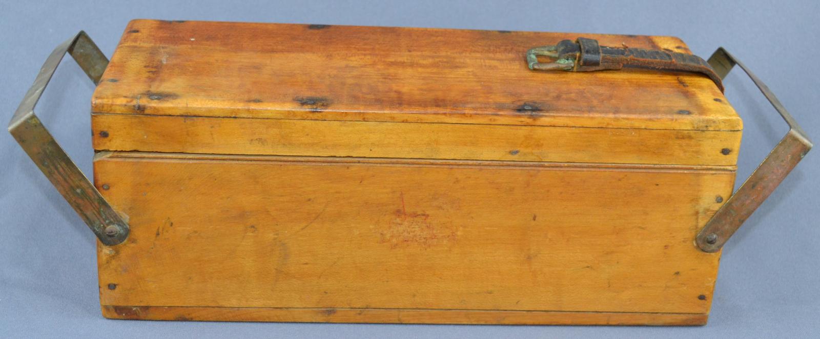 Rectangle closed light coloured closed wooden box with metal handles at each end of the box. Leather strap attached to right hand end