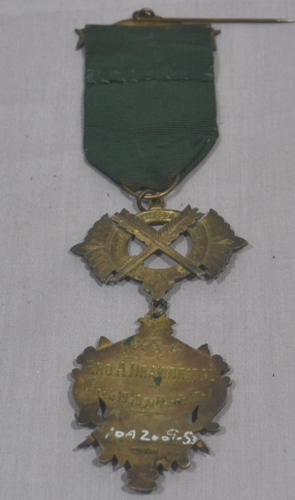 Reverse side of brass medal with green ribbon, inscription on back of medal 'Bro. A. Drawbridge / March 1950 to March 1951'