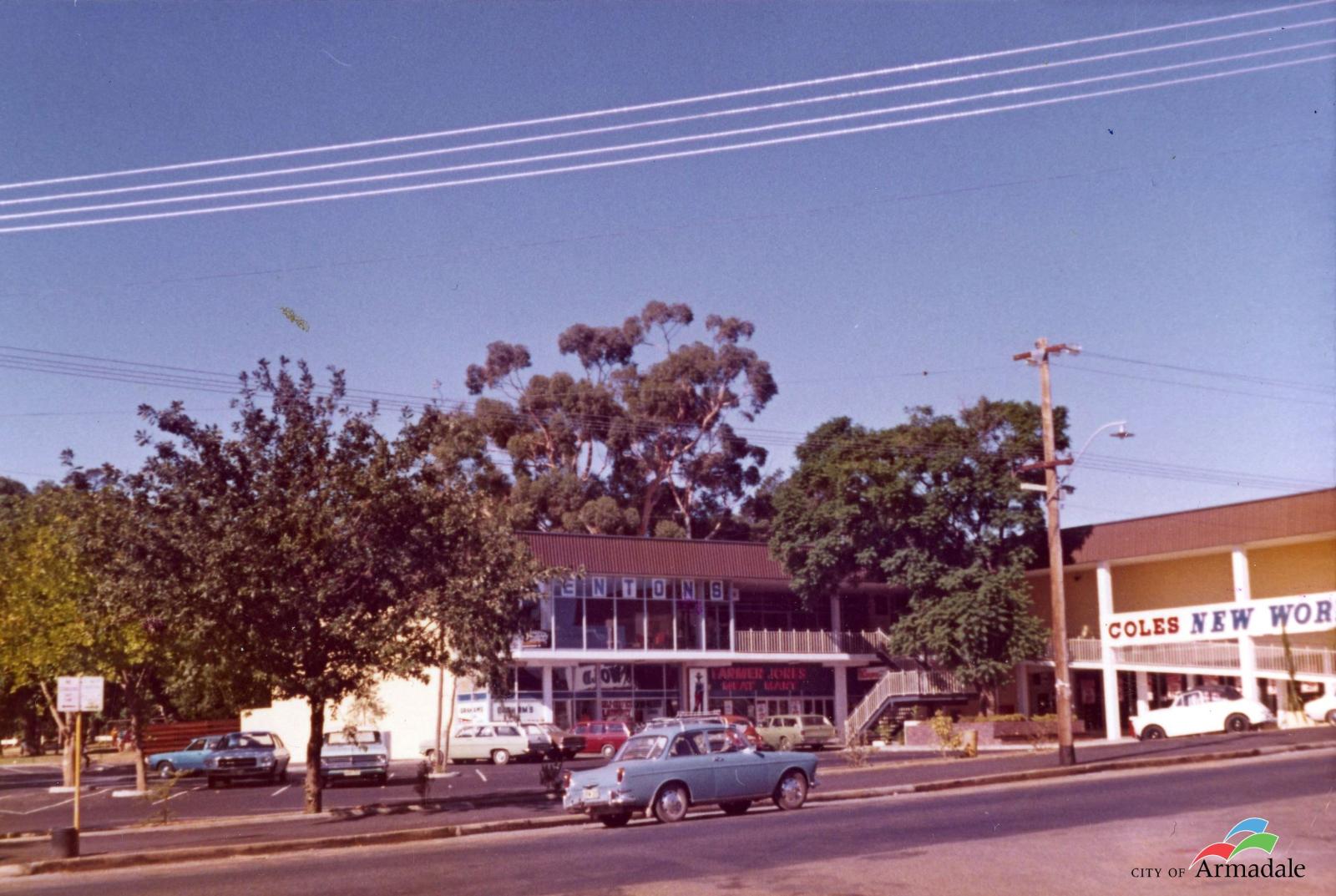 colour photograph of a two storey L shaped commercial building with cars parked at front. Sign on right part of building Coles New World