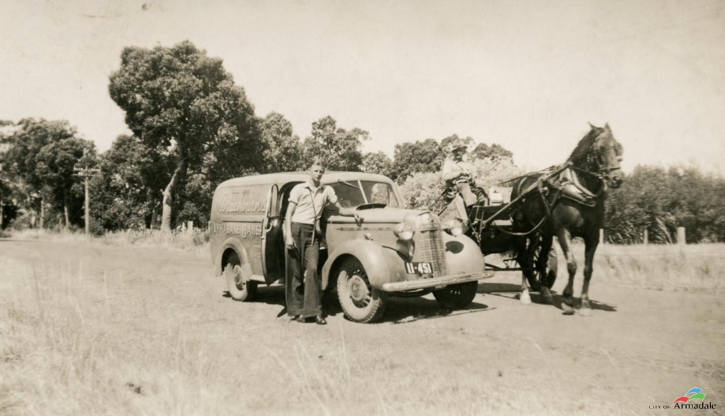 Black and white photograph of a van and a horse and cart outside on the side. The van and cart is parked on a dirt road. Text on side of van Blackburn's Armadale Bakery. Man in long pants and collard shirt standing next to van. Older man wearing a hat sitting in front of cart, holding reigns for the black horse that is hitched to the cart.