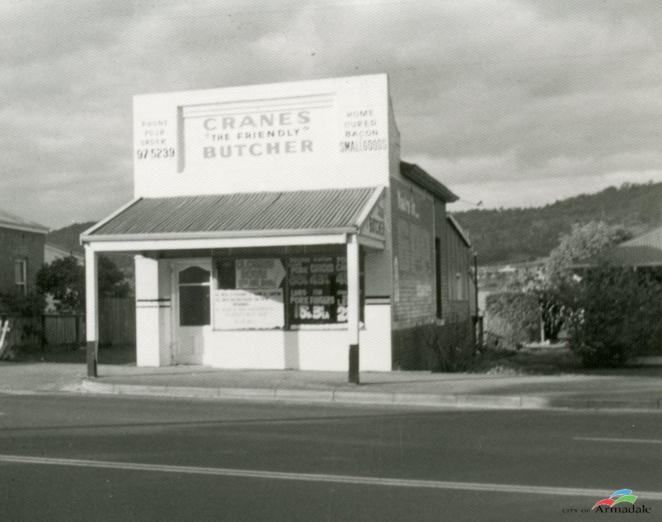 Black and white photo of a white painted single storey shop, verandah at front, sign above verandah with Crane's Family Friendly Butcher. 