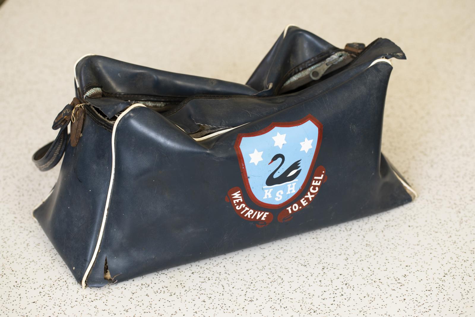 Black bag with a logo of a swan on a light blue background. Text below logo is 'KSH WE.STRIVE TO.EXCEL.''