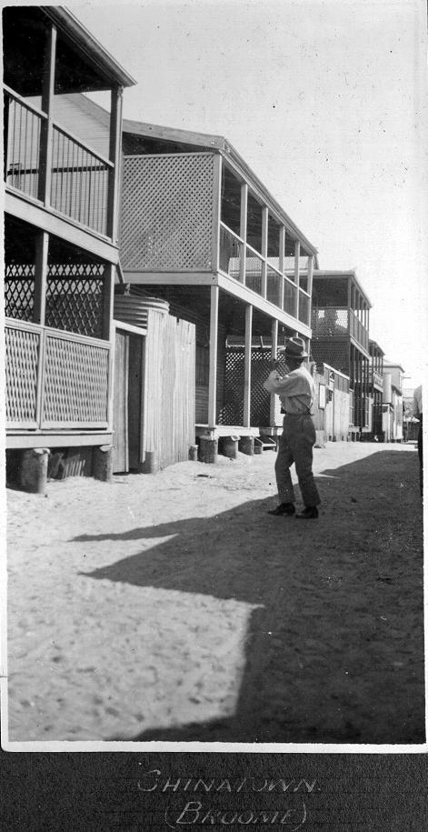 Portrait black and white photograph of man standing in street in front of buildings. 