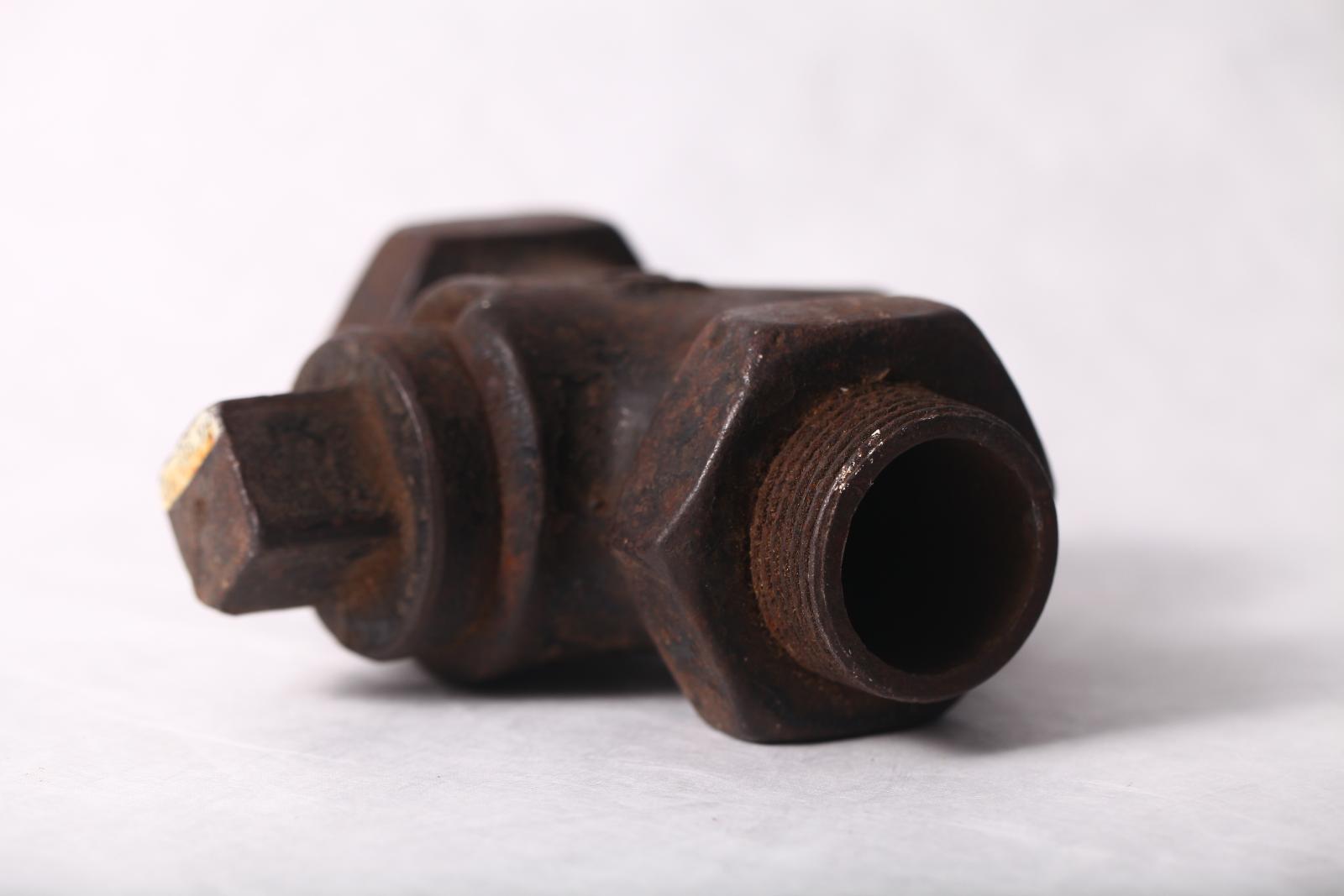 View showing the lower section of the stop cock valve with a hexagonal rim and opening with a thread on the external side, to the left is a square cast iron nut