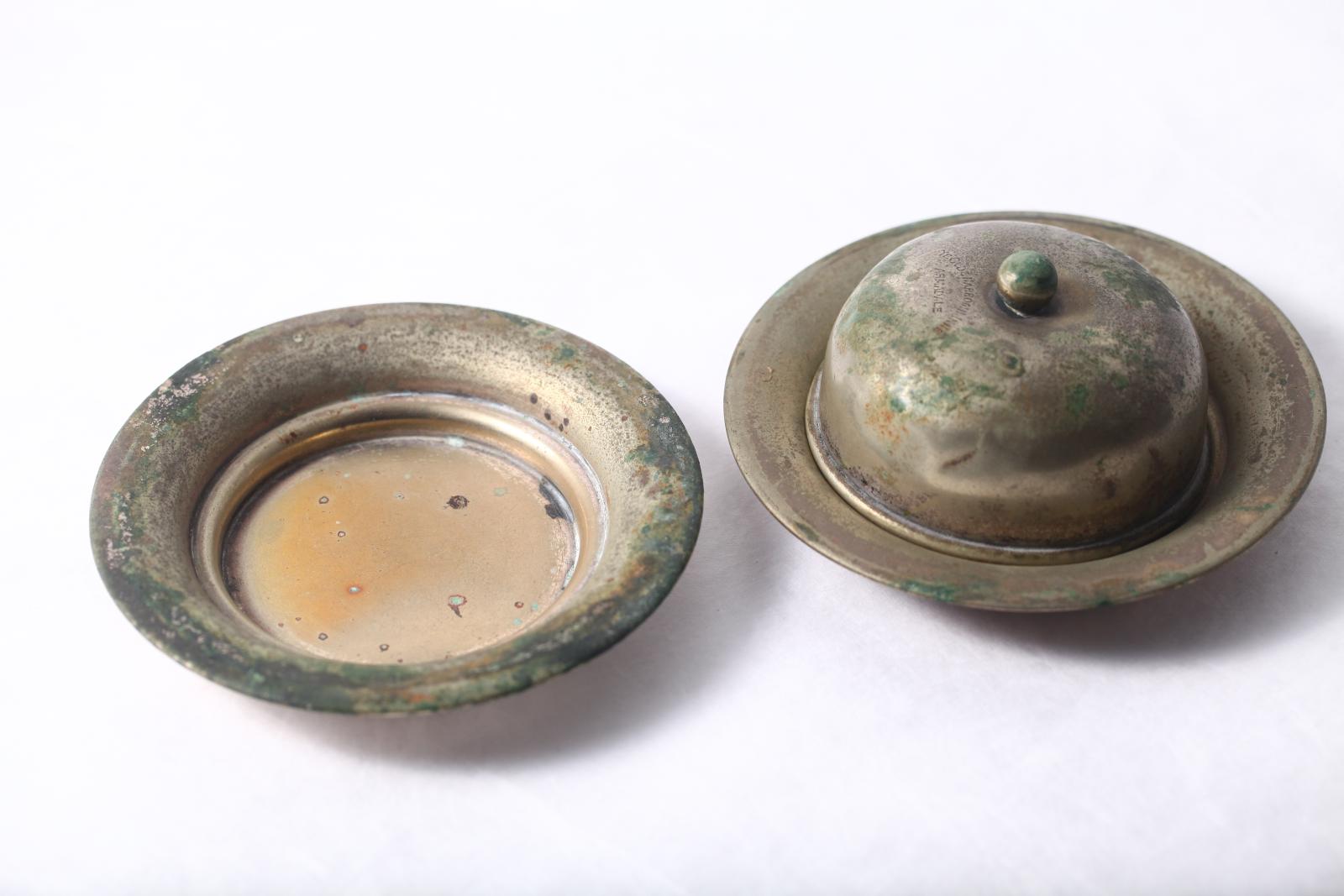 Small silver round plate from butter dish is shown on the left, while a complete plate and cover is shown on the right, both tarnished silver