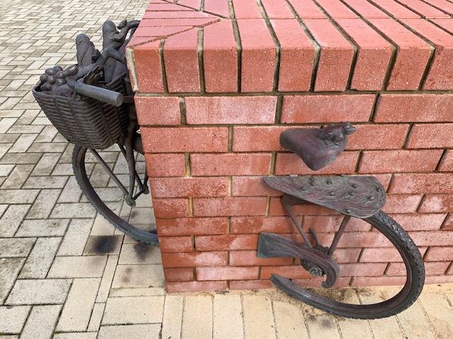 Bronze bicycle going through the corner of a brick wall