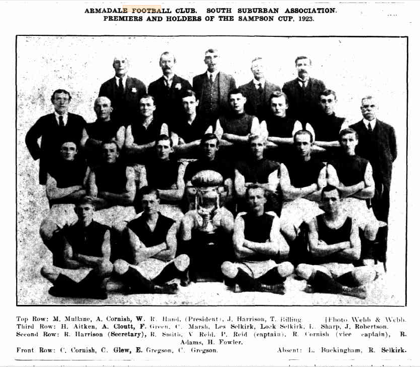 Black and White photograph of four rows of men, two standing, two seated. Front three rows most of the men are wearing football uniforms, back row and the two men at either end of the third row in suits. Man in middle of second row is holding a trophy. Under the photo is a list on names of the men who are in the photo. Photo was published in the Magpie on 9 Novemer 1923 on page 8