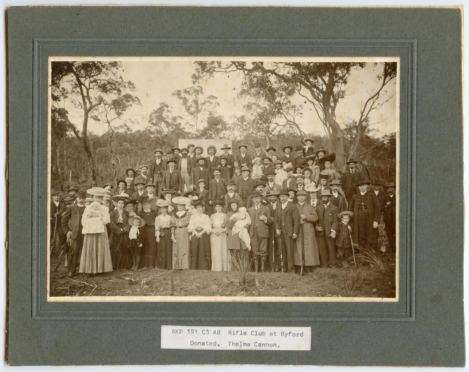 Black and white image of a large group of men and women from the early 1900s posing outside in the bush. Women are in the front row. Members of the Armadale Rifle Club 1907