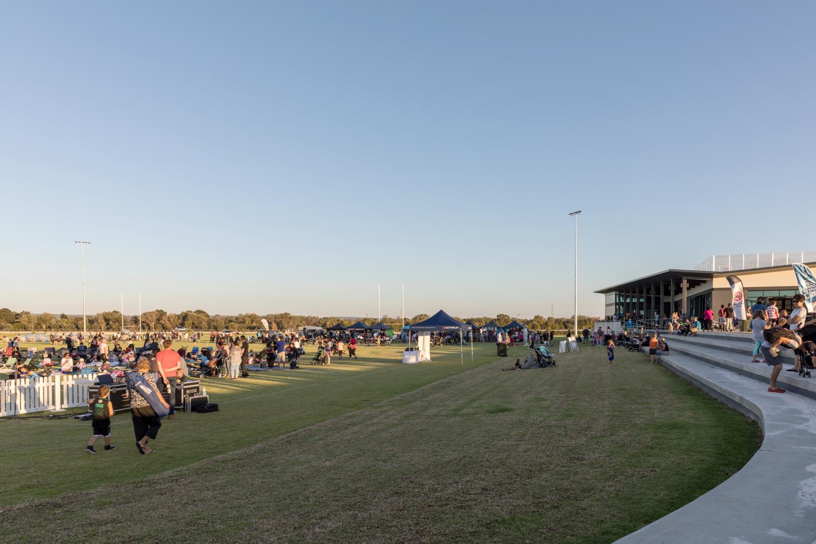 Colour photograph of people walking and standing outside of the new Harrisdale Pavillion which over looks a grass oval.