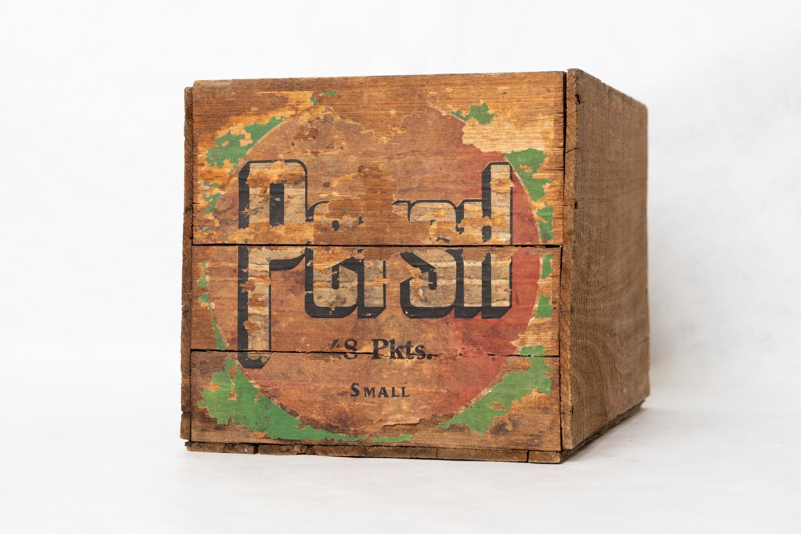 Square wooden packing box with the inscription in black and white 'Persil 48 Pkts. SMALL' on a red circle with a green background.