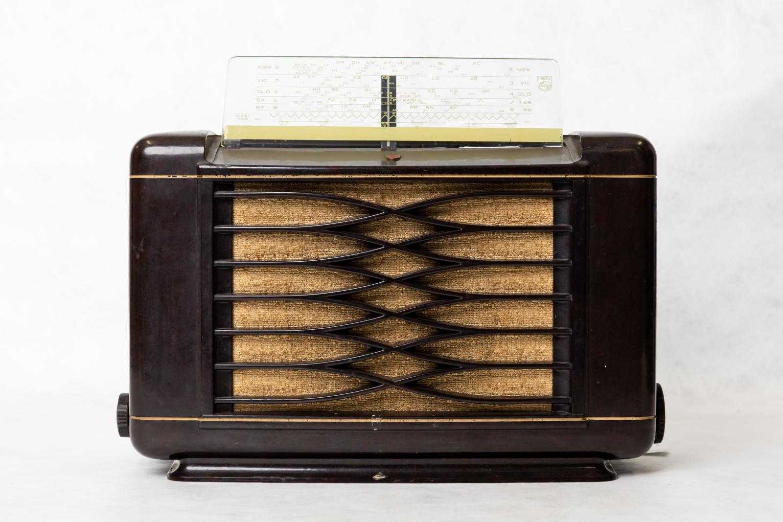 Dark brown, rectangular shaped, short wave mantle radio with clear plastic and yellow station selector on the top. Open grid with diamond pattern in the centre, filled with light brown cloth. 