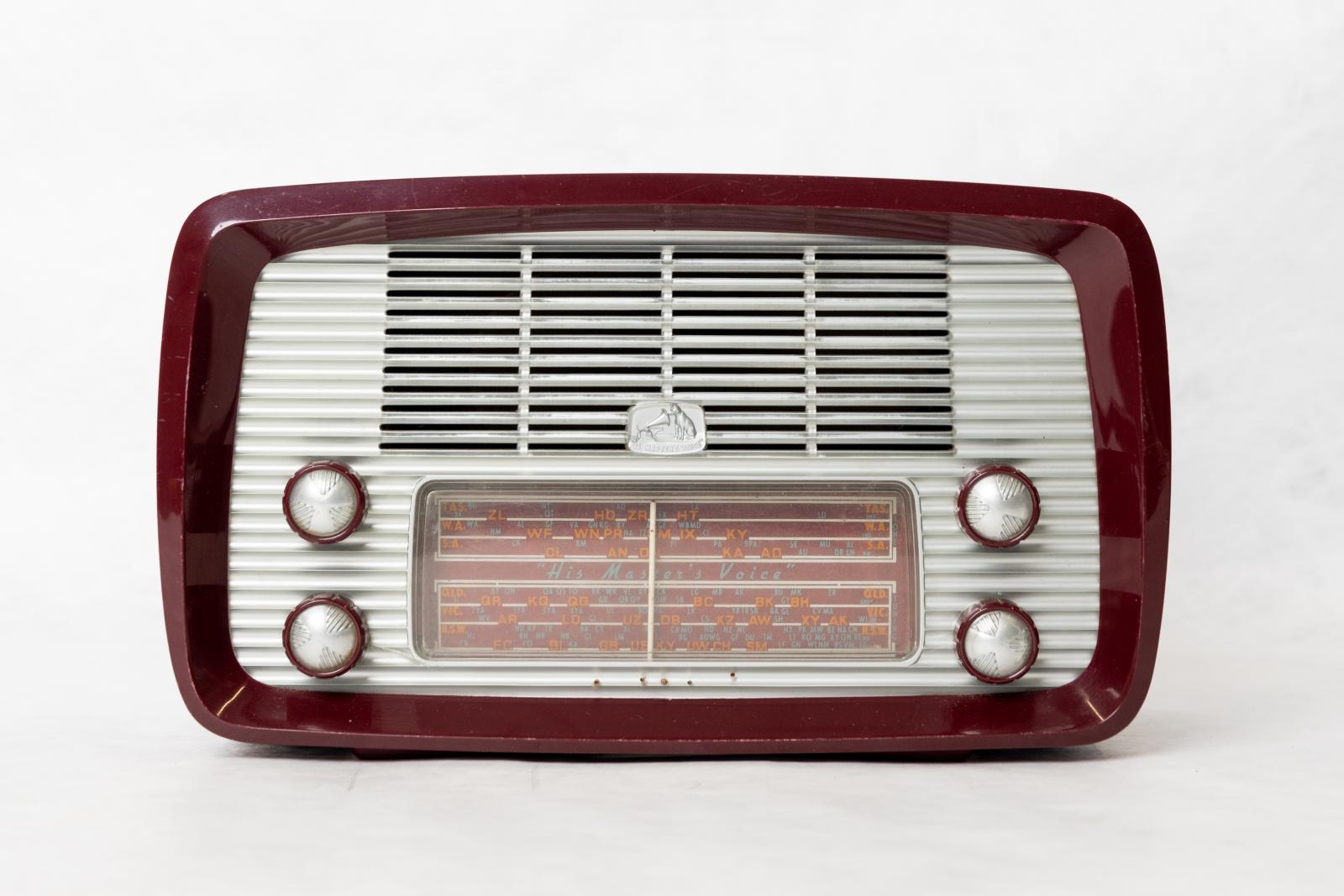 His Master's Voice rectangular box shaped, short wave mantle radio, with curved edges. Burgundy Bakelite casing with curved edges, clear plastic with silver backed front with horizontal speaker grill with tuning panel below. Two burgundy tuning dials on each side with silver plastic centres with triangular moulded design. 