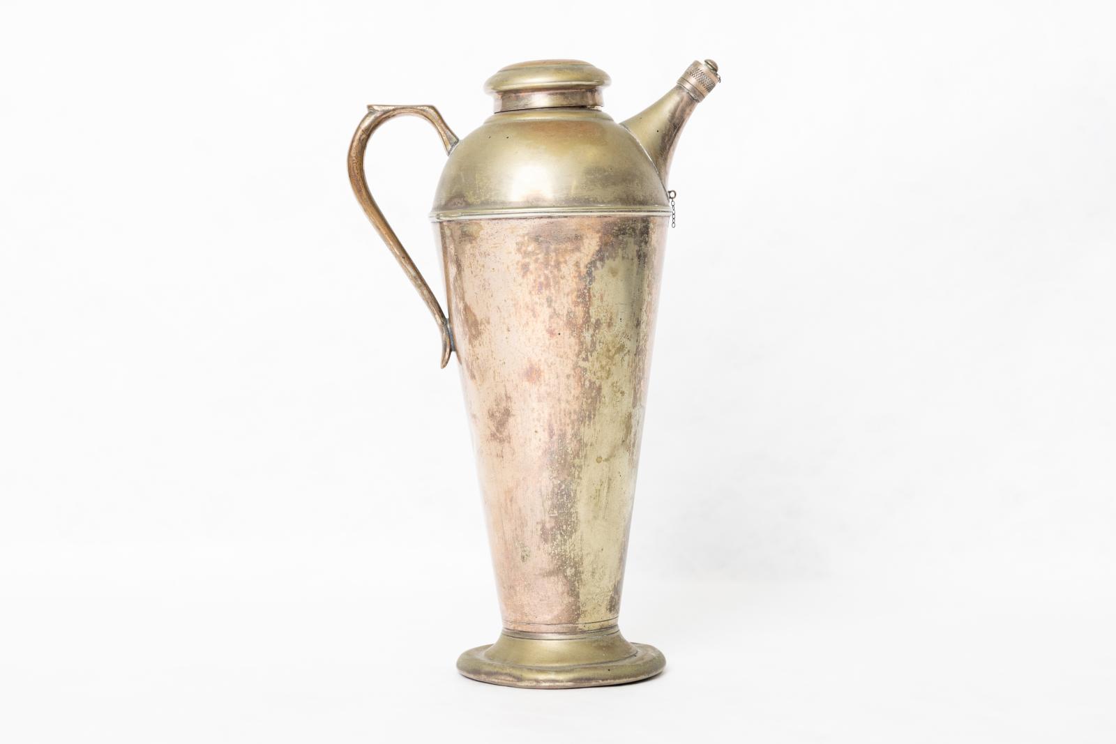 Gold nautical style coffee serving jug with broad flared base and circular domed tight fitting lid and small cross hatched screw on cover for spout. Shape of container narrow at bottom and elongated with a domed section at top where spout and handle are attached. Fine link chain segments on lower section of spout and on detachable spout cover. 