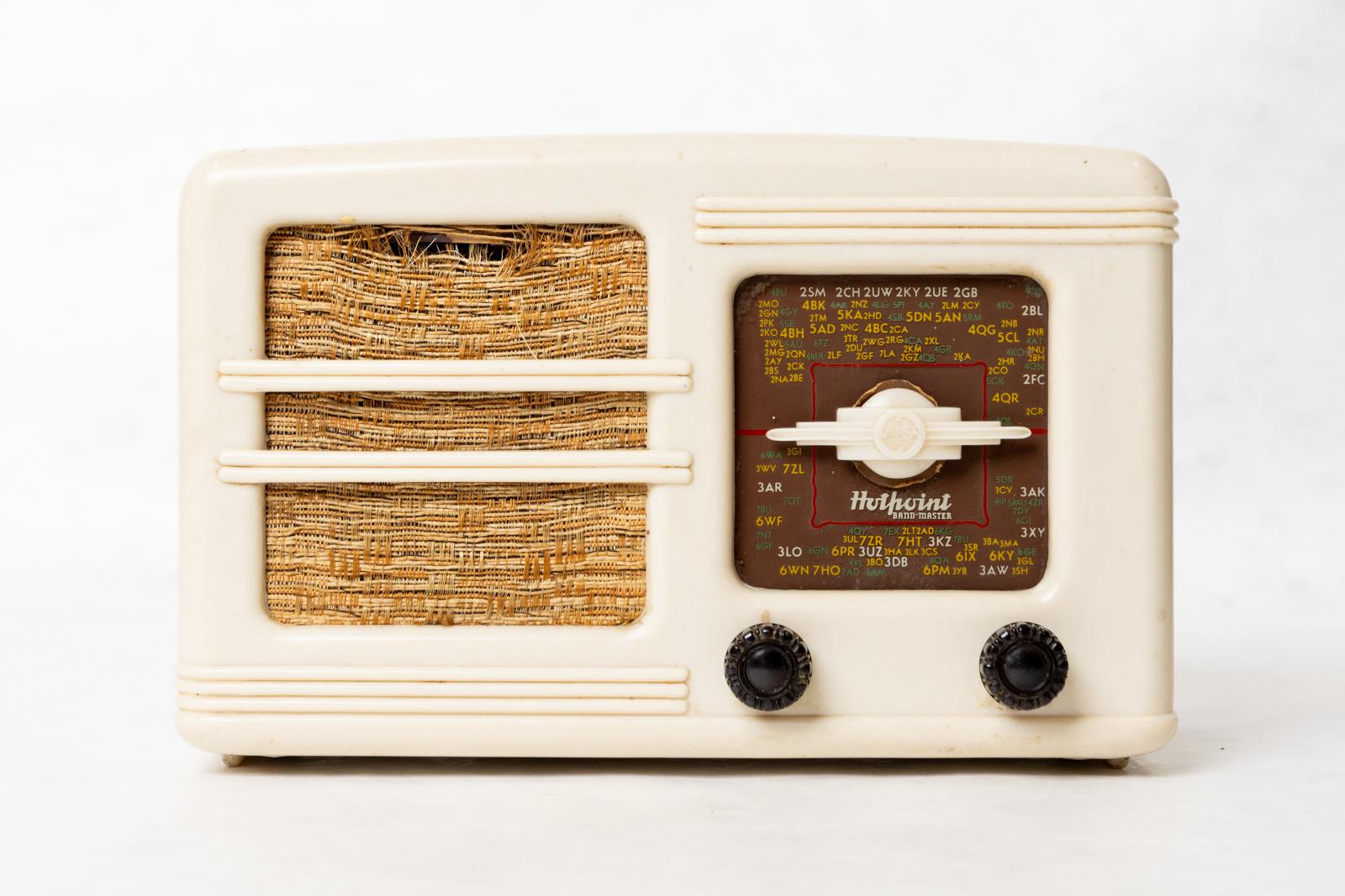 Short wave radio. Rectangular box, ivory Bakelite, Art Deco style casing. Light brown and cream woven grille cloth with square glass tuning panel and two dark brown round Bakelite tuning knobs below panel. Horizontal design features lineal lines grouped in 2 and 3, with cream planet shaped Bakelite tuning indicator in centre of glass panel.