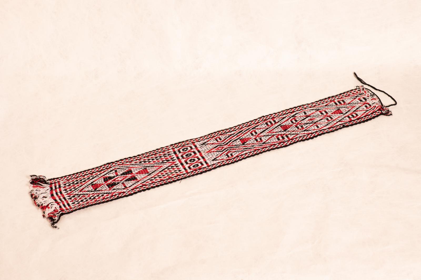 Woven cotton belt or waistband with fringed ends and red, black and white triangular geometric pattern.