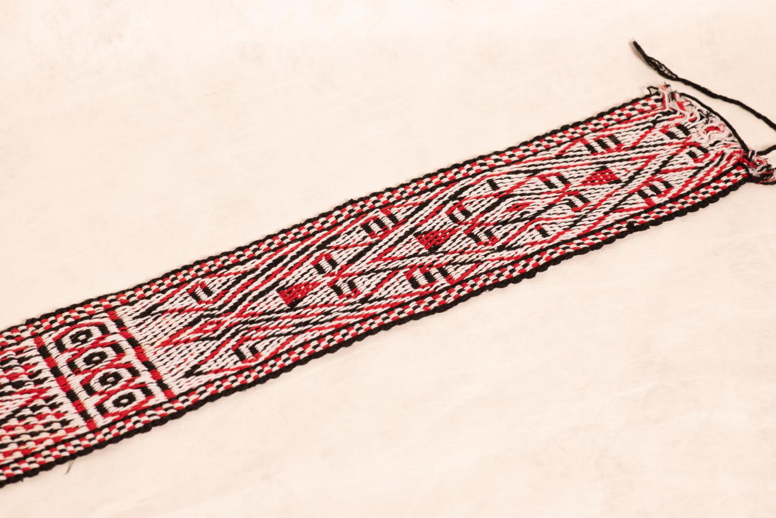 Woven cotton belt or waistband with fringed ends and red, black and white triangular geometric pattern.