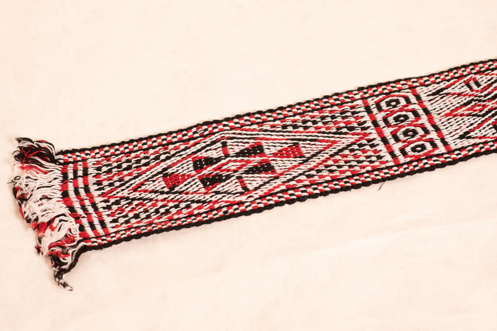 Woven cotton belt or waistband with fringed ends and red, black and white triangular geometric pattern.