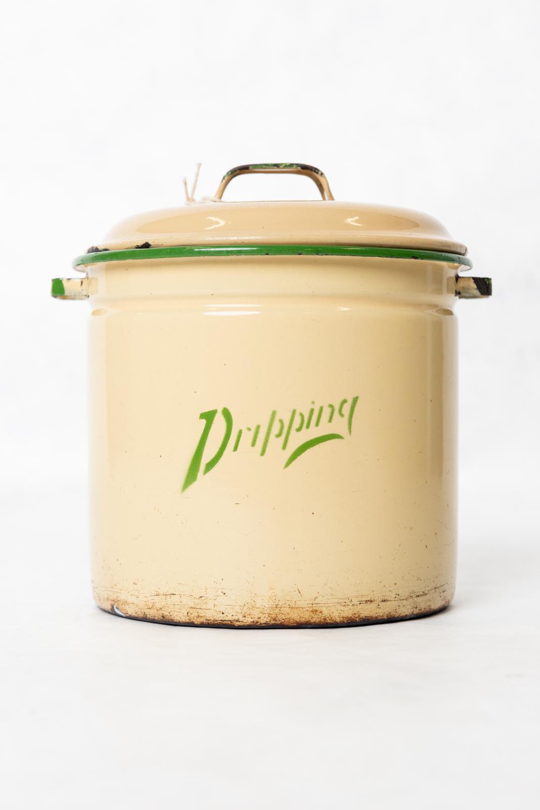 Cylindrical, metal, cream coloured, enamel 'Dripping' container. Round base with tall sides with a rounded green enamelled rim. A small thin, square, green enamelled handle, is welded to each side. On the front in the middle of the canister at a slight angle, painted green is the word 'Dripping'. Cream enamelled, tin lid. Narrow rim around the edge. The lid then curves upwards with another shallow circular ridge around the middle. In the centre, on top of the lid, is a small, square, green enamelled, handle