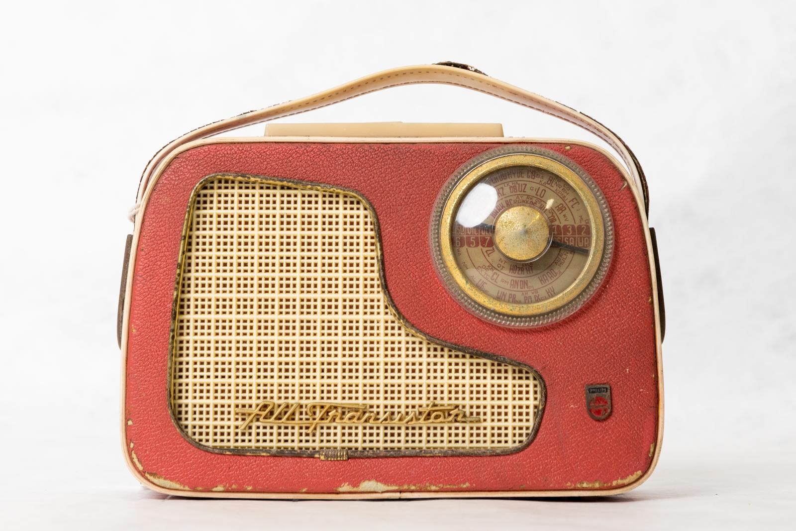 Rectangular, red and cream, plastic and leather, Philips, 'All Transistor', portable radio. A clear round station dial in the top right hand side and a cream carry handle at the top.