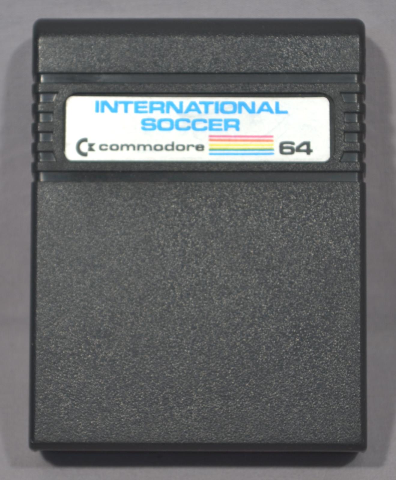 Black rectangular cartridge with the top edge rounded. Five ridges run around the cartridge near the top, with a silver coloured rectangular label with blue printing of International Soccer