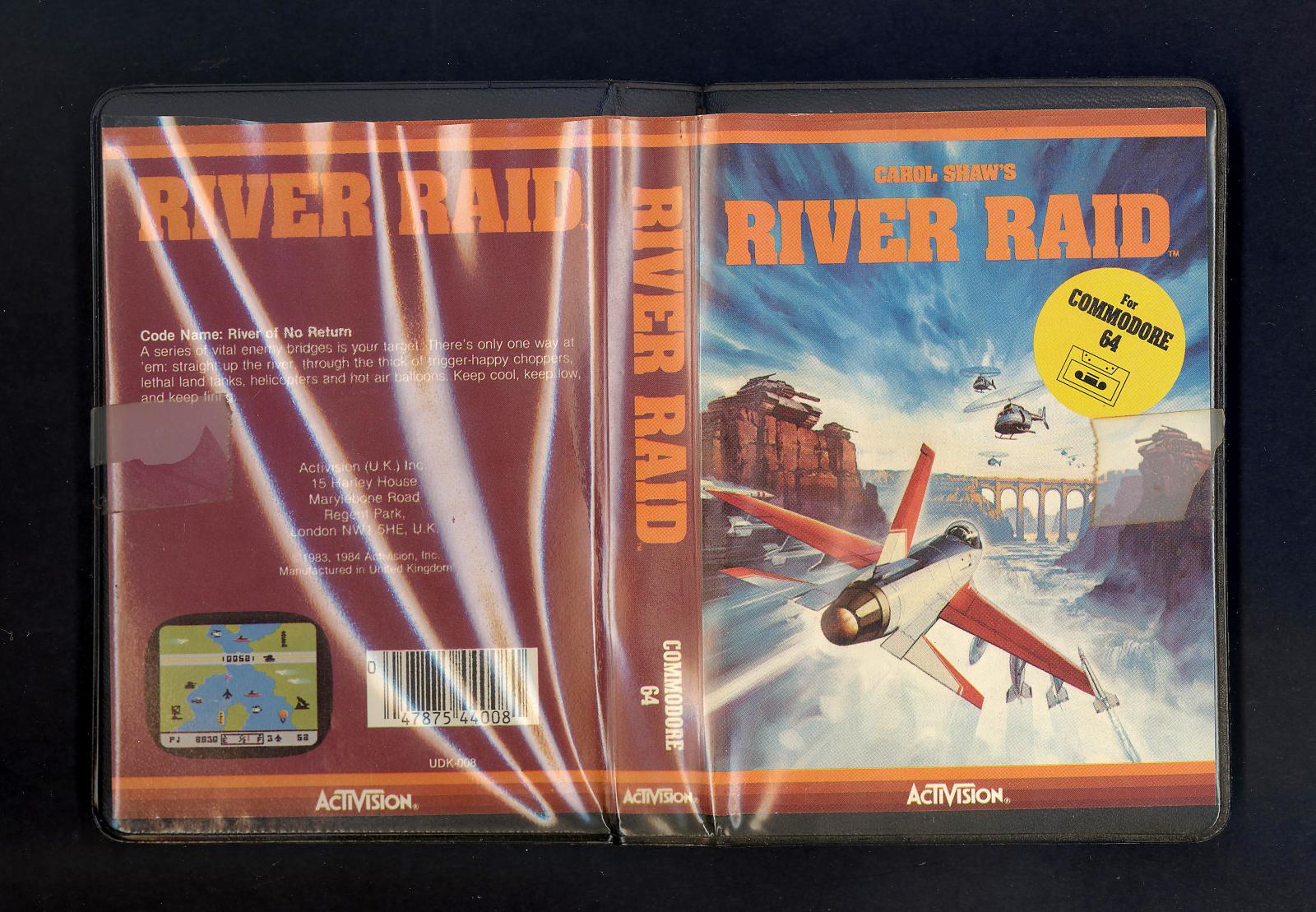 View of both front and back covers of River Raid Game. The package is made of hard black plastic and has a sleeve of clear soft plastic around the outside. A paper insert is in this sleeve, with the game title and details.