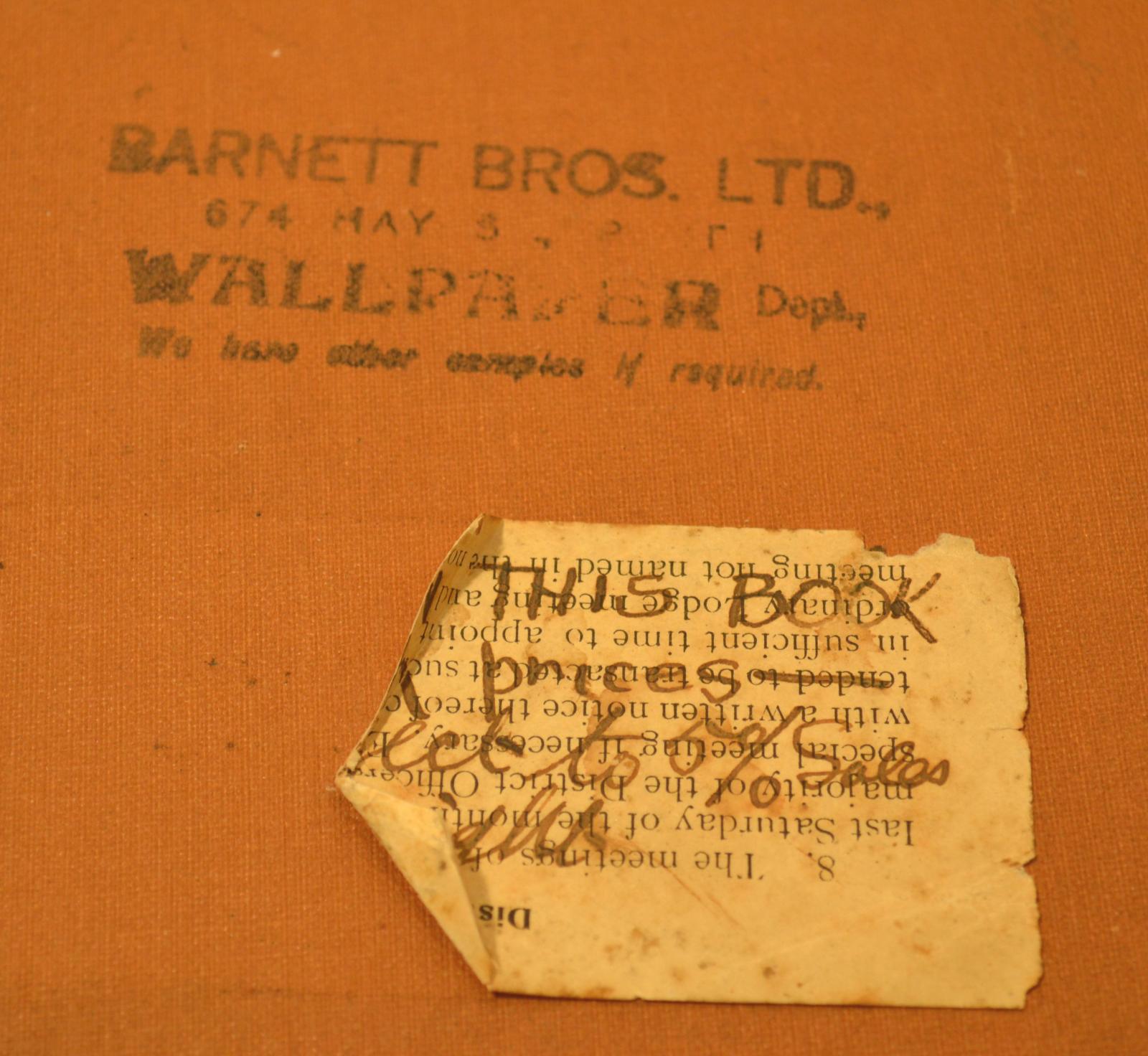 Close up photograph of stamped text and text written on a white label on front cover of the wall paper sample book