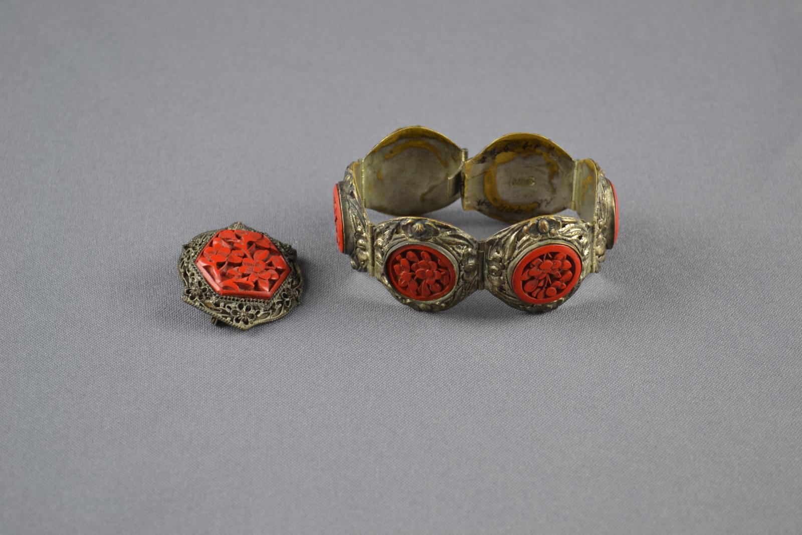 Metal bracelet with round red carved cinnabar inserts. Next to the bracelet is a broach of the same design and material