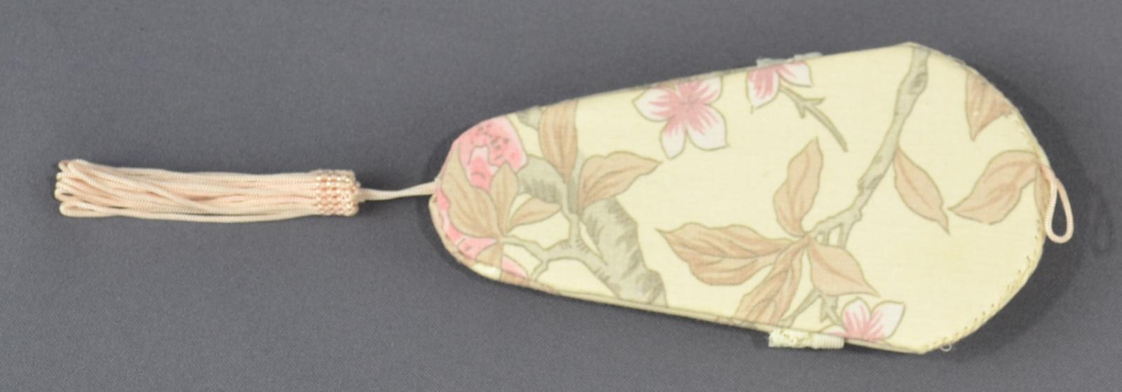 A pale lemon coloured fabric with a printed tree/leaf/flower pattern covers the back of the pouch. A puce coloured tassel is attached to the lower edge