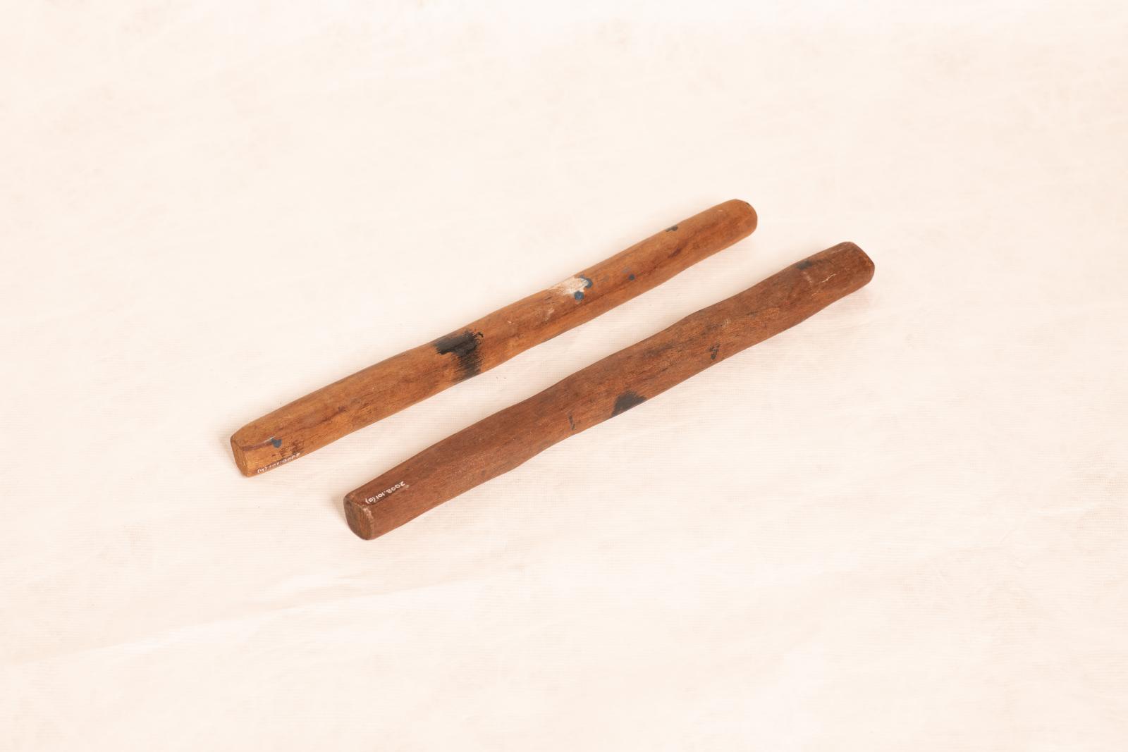 Pair of dark wood clapping sticks, thin elongated shape with rounded sides and painted linear pattern near centre.