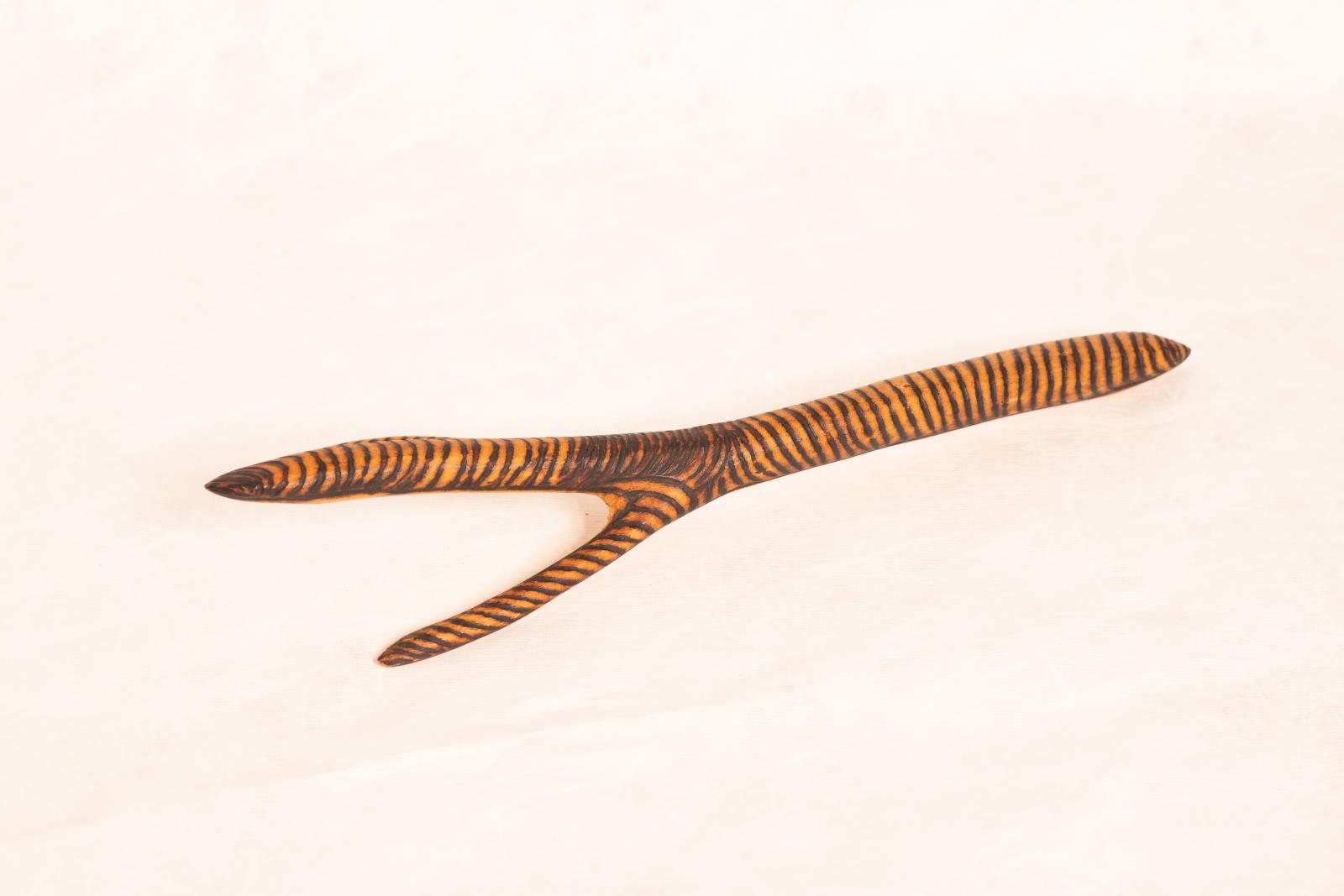 Carved beige wooden emu foot with two thin projections and thicker central projection, and longer leg shape. Along length of carving rings are burnt into the wood.