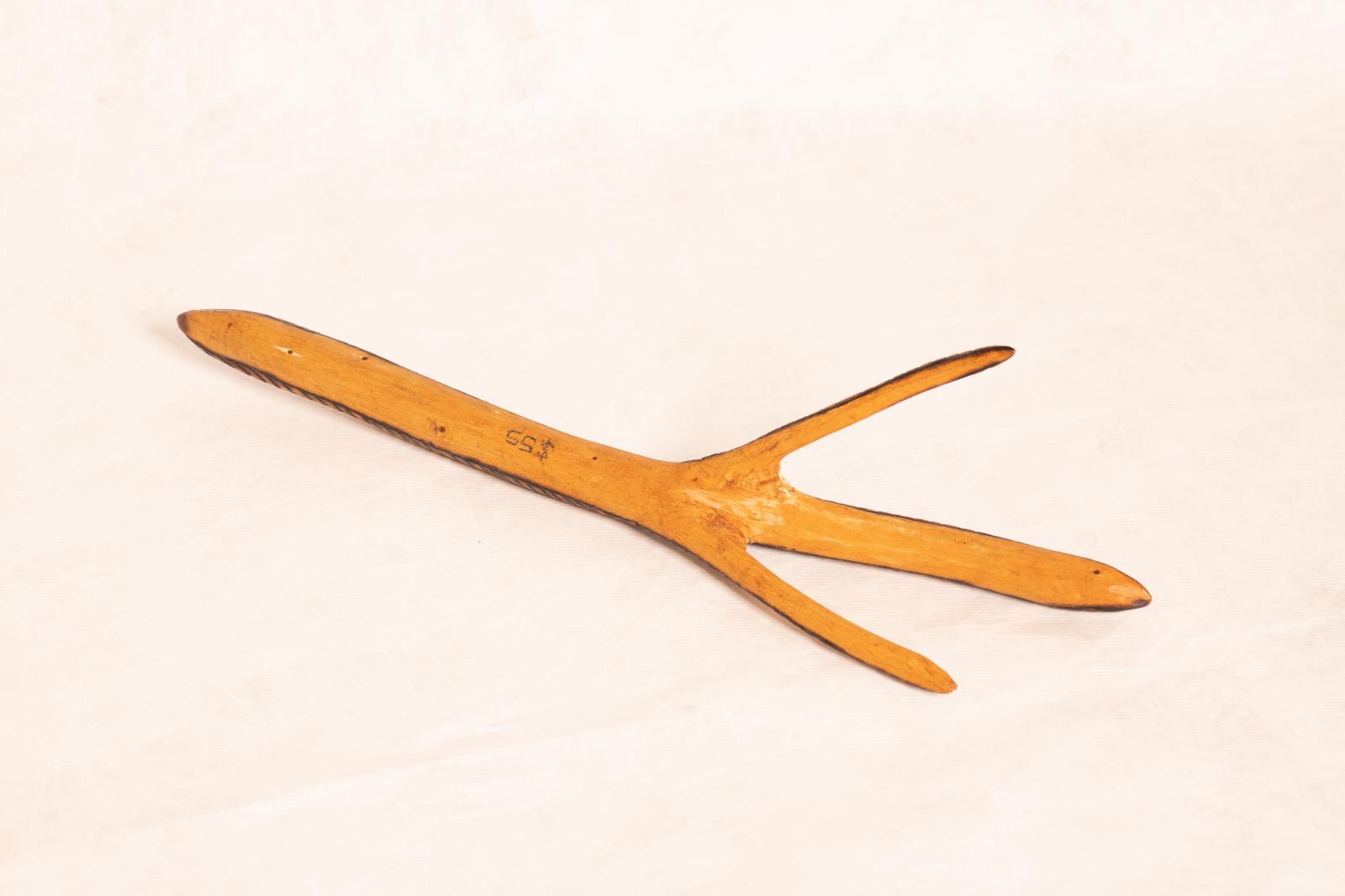 Carved beige wooden emu foot with two thin projections and thicker central projection, and longer leg shape. Along length of carving rings are burnt into the wood.