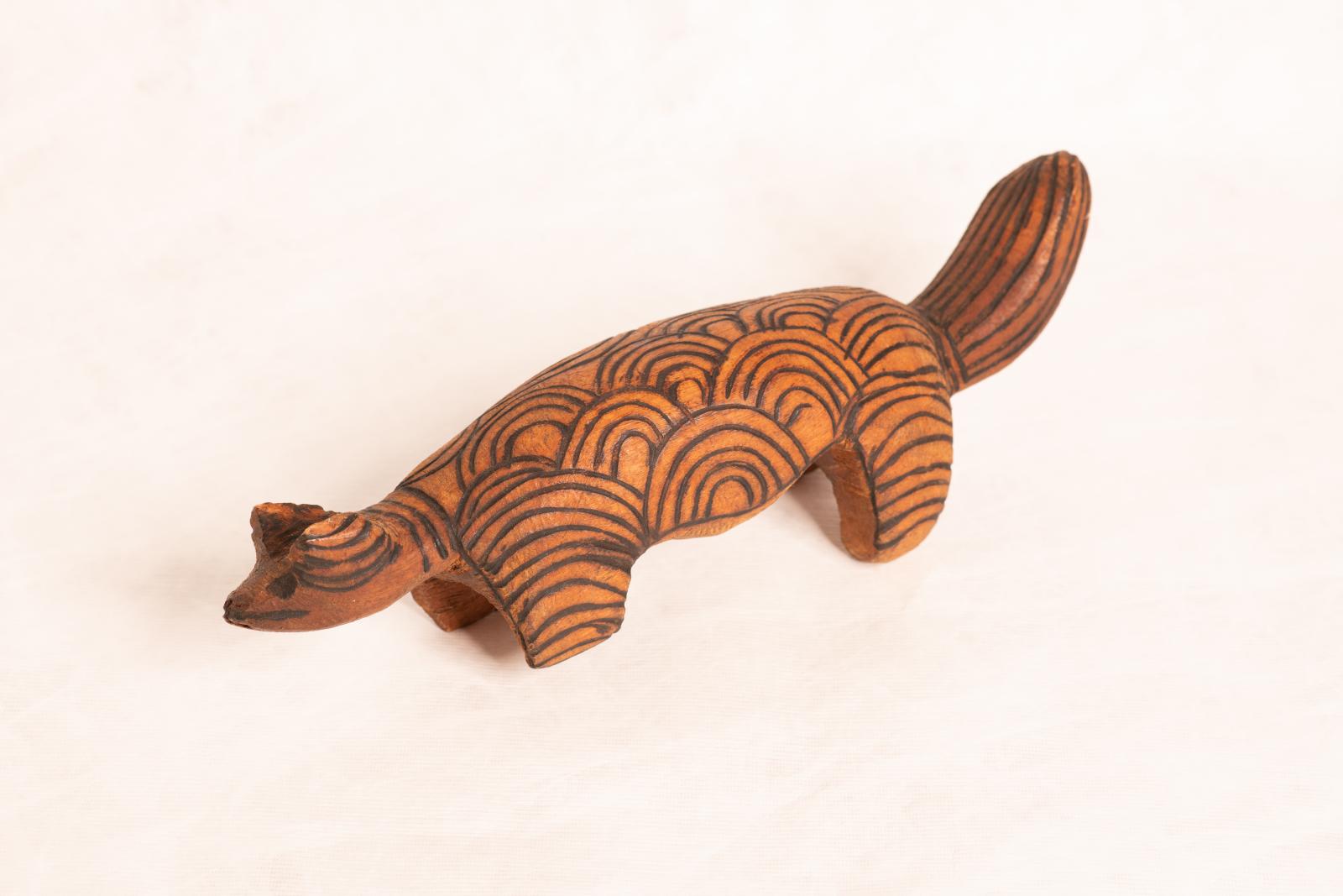 Large carved dark wood animal figure, large round body with round flat tail and small round head. Circular pattern is burnt into the surface.