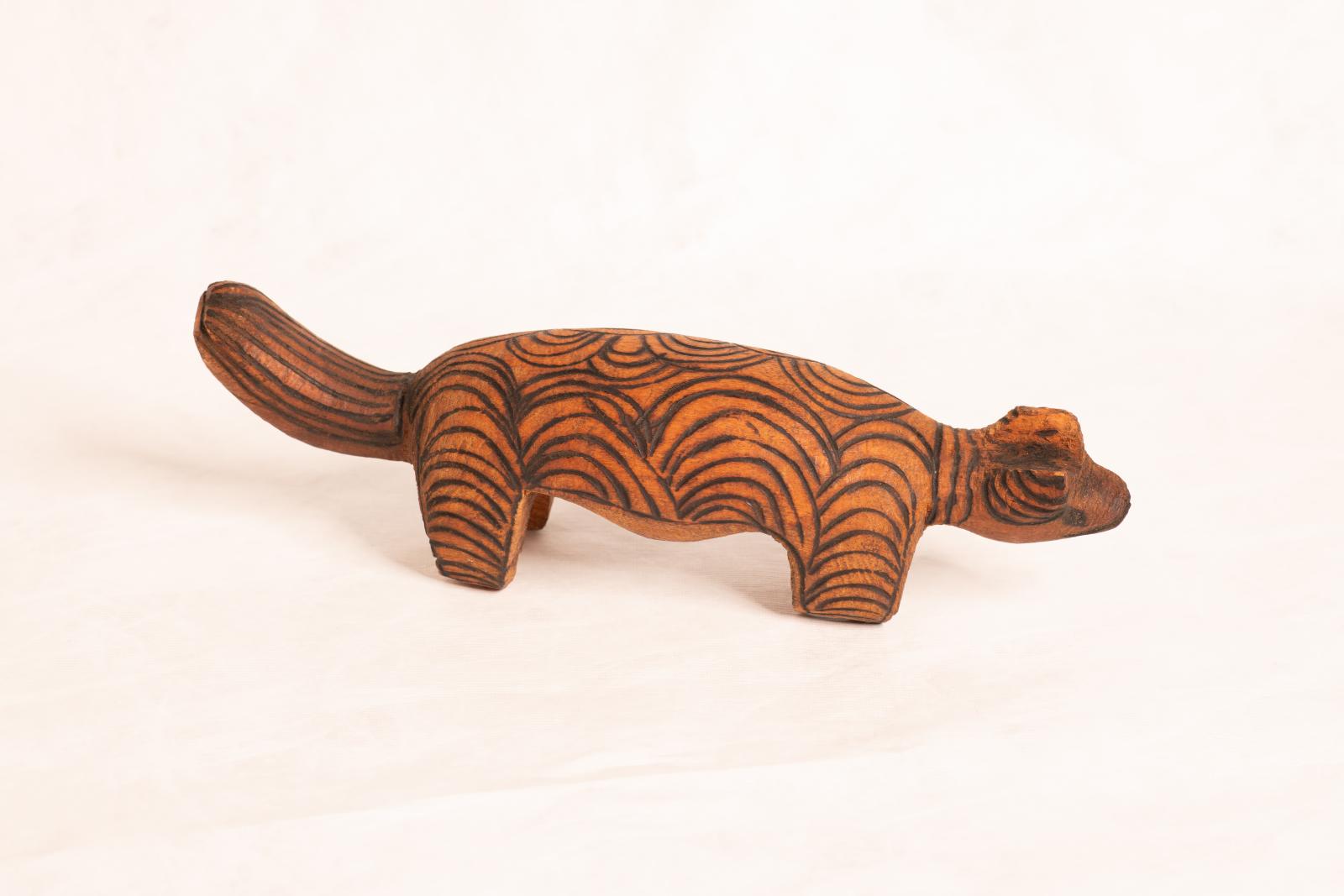 Large carved dark wood animal figure, large round body with round flat tail and small round head. Circular pattern is burnt into the surface.