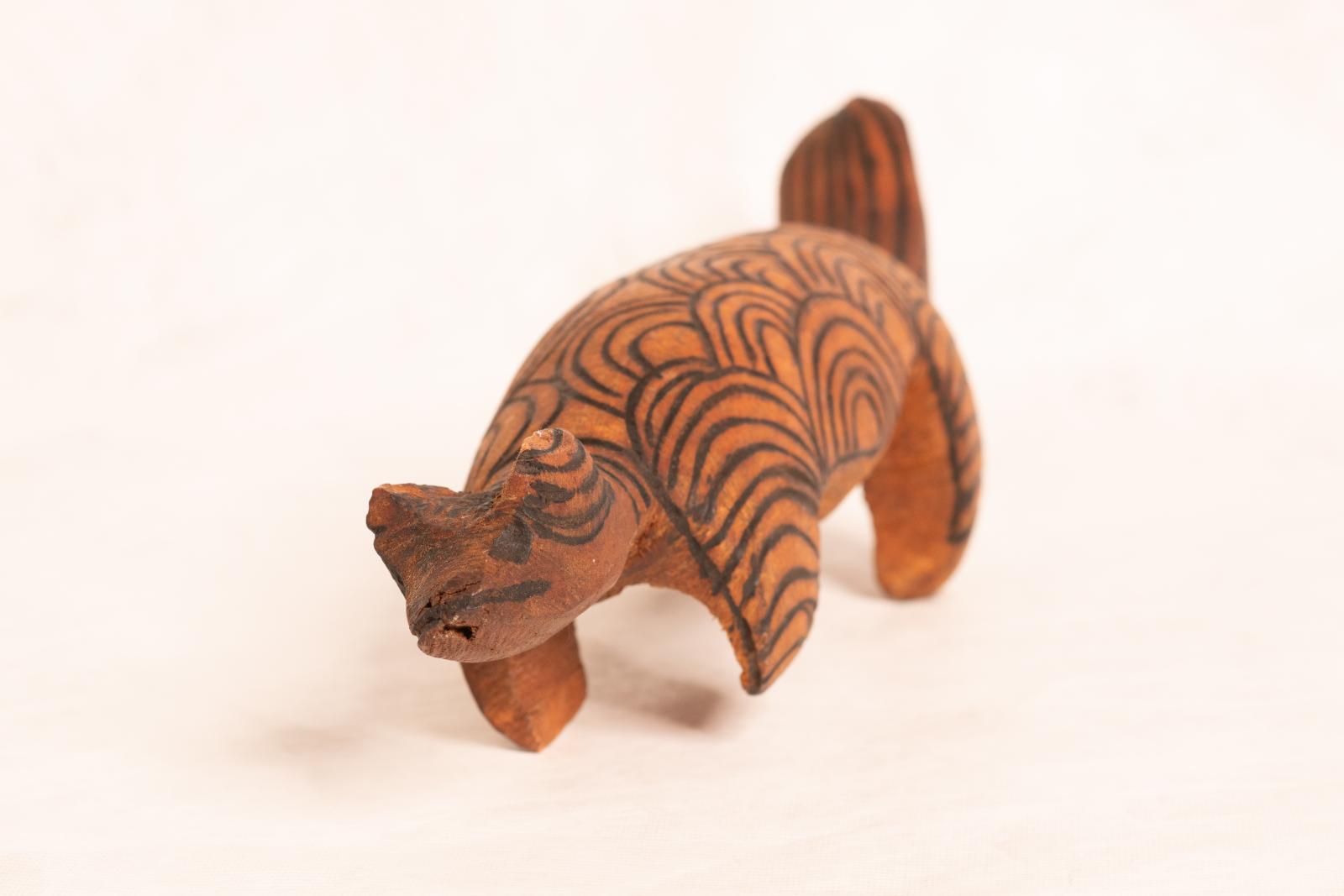 Large carved dark wood animal figure, large round body with round flat tail and small round head. Circular pattern is burnt into the surface.