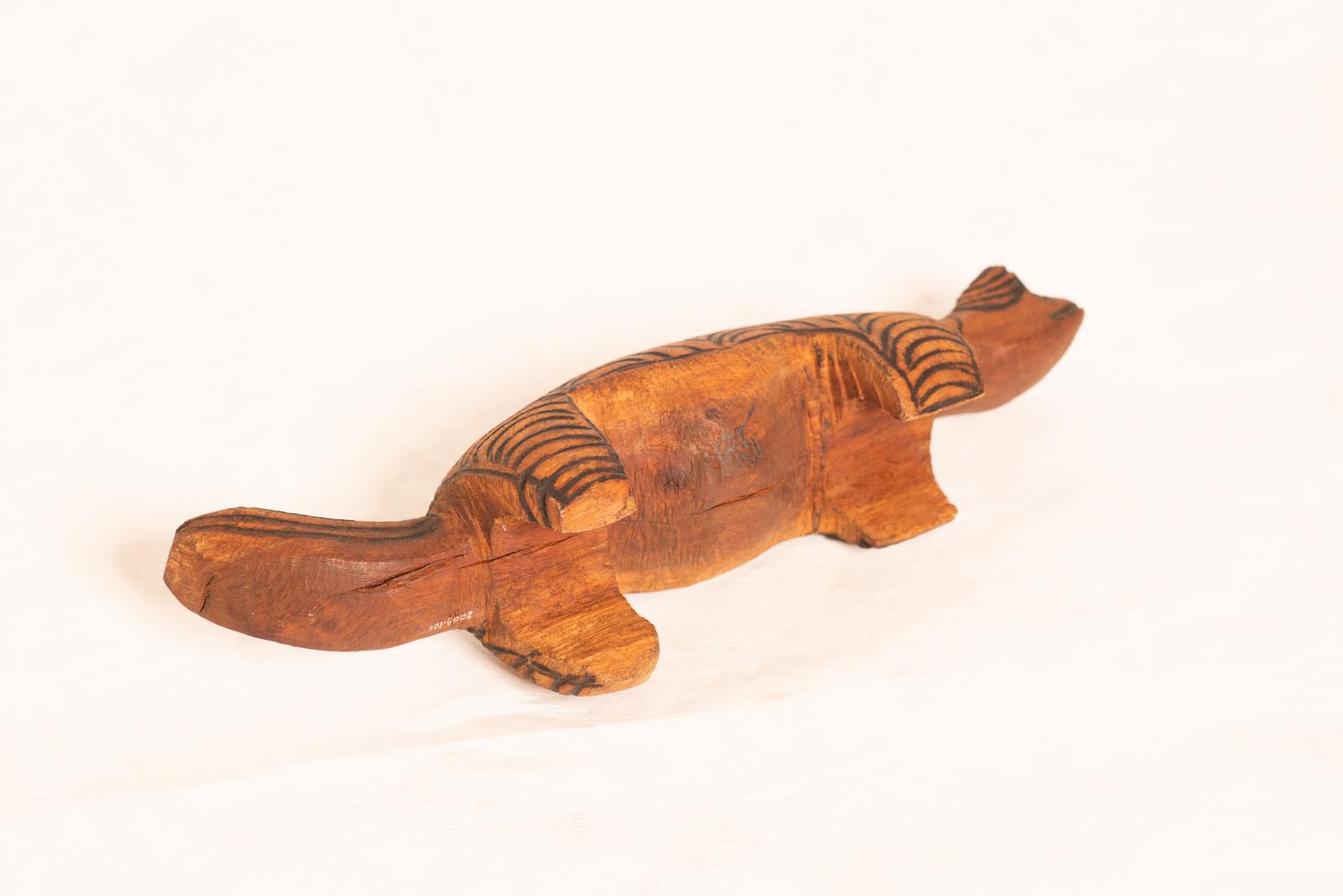 Large carved dark wood animal figure, large round body with round flat tail and small round head. Circular pattern is burnt into the surface.