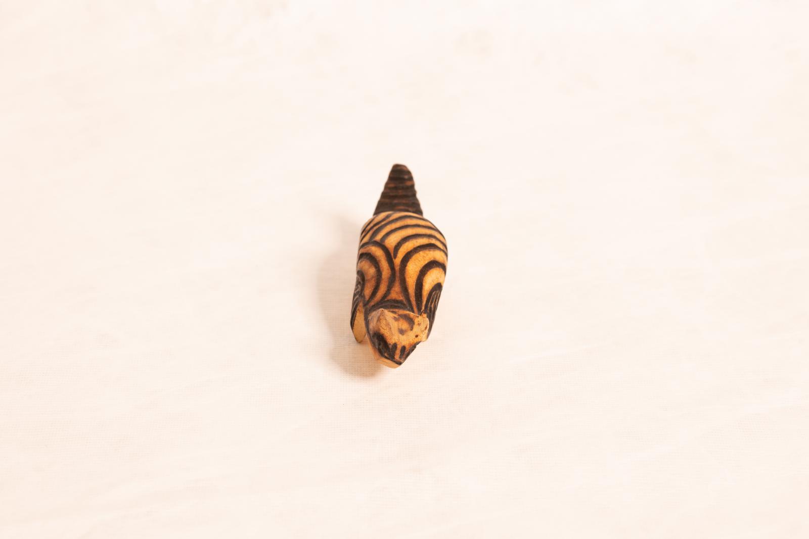 Small carved beige wooden animal figure, large round body with small pointed tail and round head. Circular lined pattern burnt into surface.